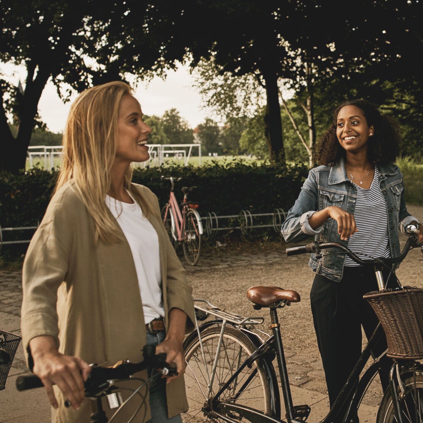 Two women with bicycles smiling outdoors near park trees in Keith, Scotland