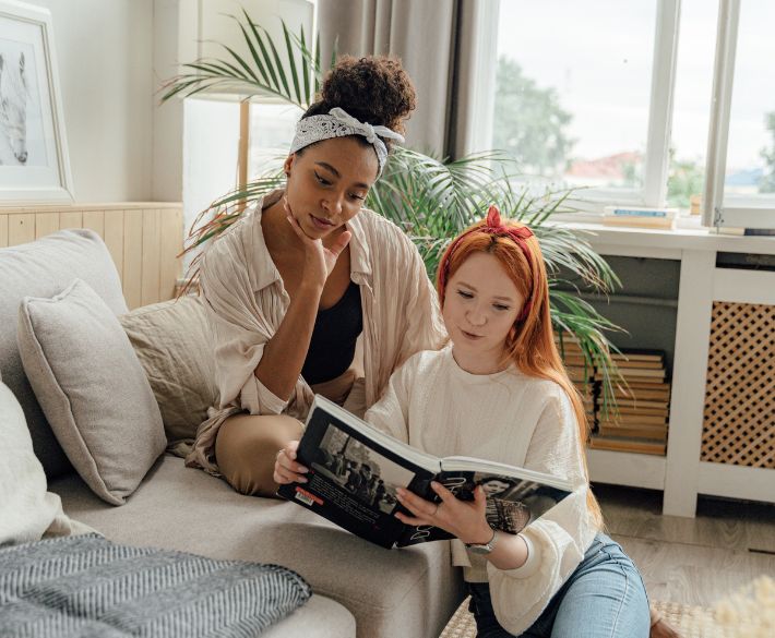 Two women sitting on a couch reading a magazine together – symbolizing shared moments, media visibility, and connection through Gofrendly