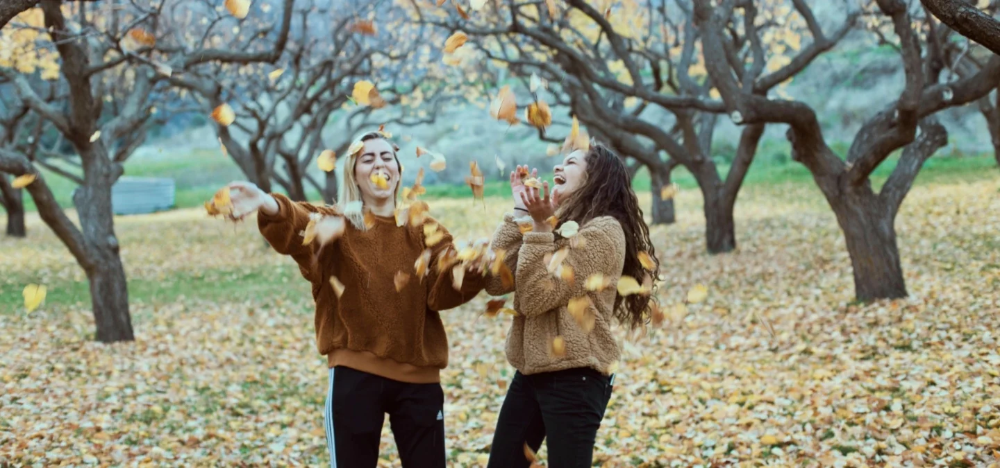 Reconnect with old friends: two women laughing and throwing autumn leaves in an orchard