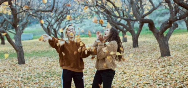 Reconnect with old friends: two women laughing and throwing autumn leaves in an orchard