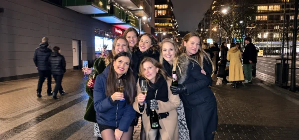 Seven women smiling together with glasses of bubbly on a city street at night