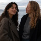 Two women standing together on a beach beside the sea.