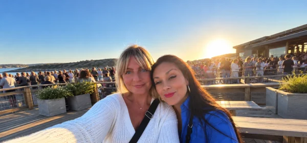 Two women taking a selfie together on a waterfront terrace at sunset.