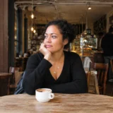 Is it normal to not have friends: a woman sitting alone at a café table with a cup of coffee, lost in thought