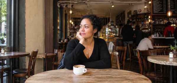 Is it normal to not have friends: a woman sitting alone at a café table with a cup of coffee, lost in thought